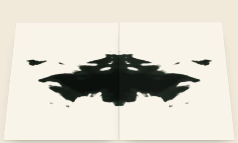 A sheet of paper lying open in perspective with a mirrored ink blot across its crease